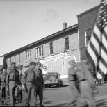 Mauston Boy Scouts enter the parade line, circa 1943. The town's military honor roll can be seen on the side of the building.